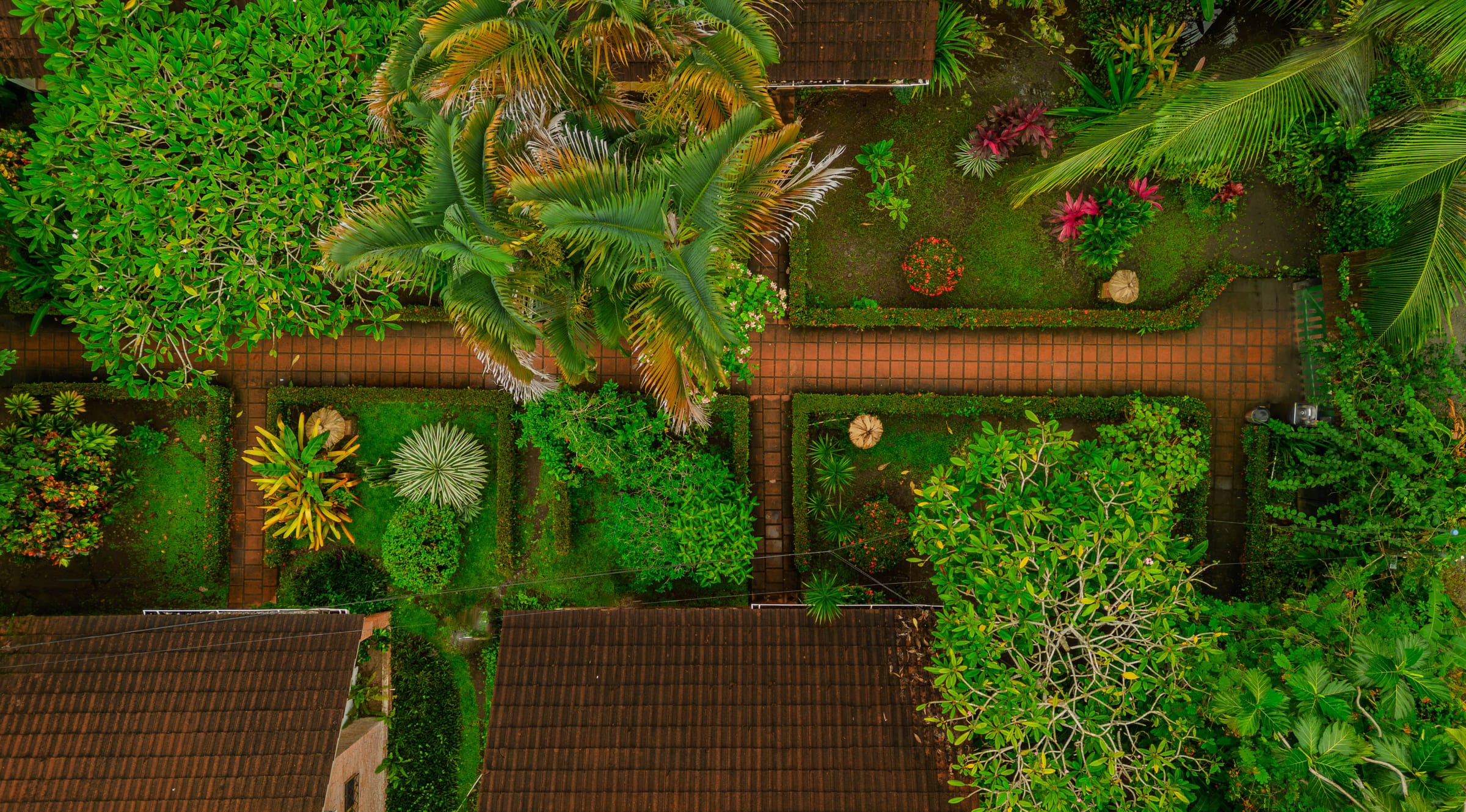 Aerial view of the property's tropical gardens, hedges, and brick pathways between two red-tile roofed buildings