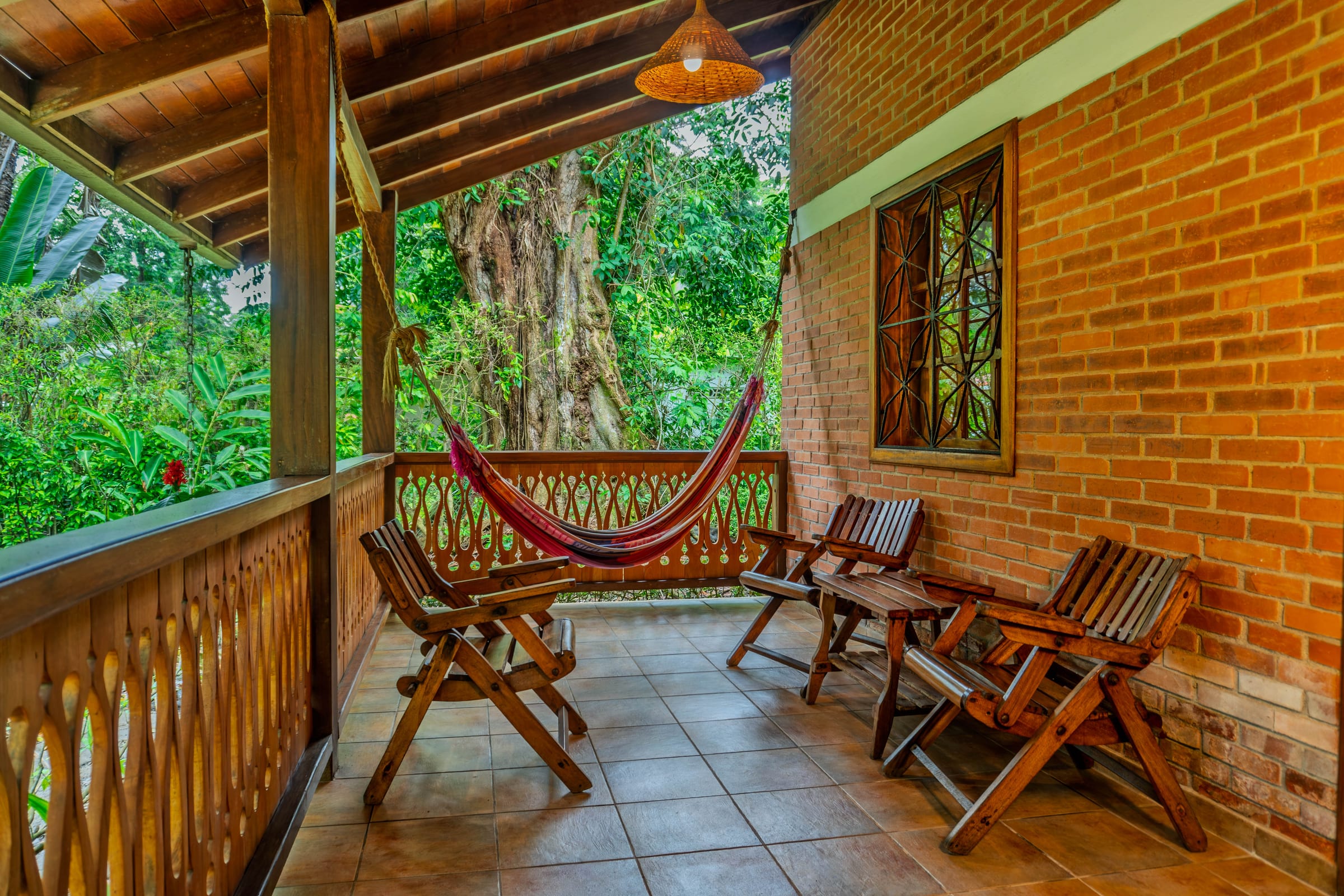 Covered brick porch of the Lado Mar room with a red-striped hammock strung between wooden chairs, overlooking a large tree